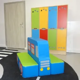 Kolorowy, miękki zestaw mebli w kształcie autobusu na dywanie imitującym ulicę w pokoju zabaw.