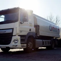 Cysterna DAF z logo firmy ATH Hernik, z pomarańczową tablicą ostrzegawczą ADR, stojąca na brukowanym placu w słoneczny dzień.