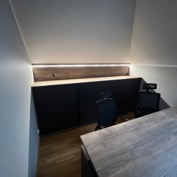 4Mat Meble na wymiar - Szafa wnękowa z czarnymi frontami i drewnianym blatem, podświetlona listwą LED, wkomponowana w skos dachu, z biurkiem i krzesłami biurowymi.
