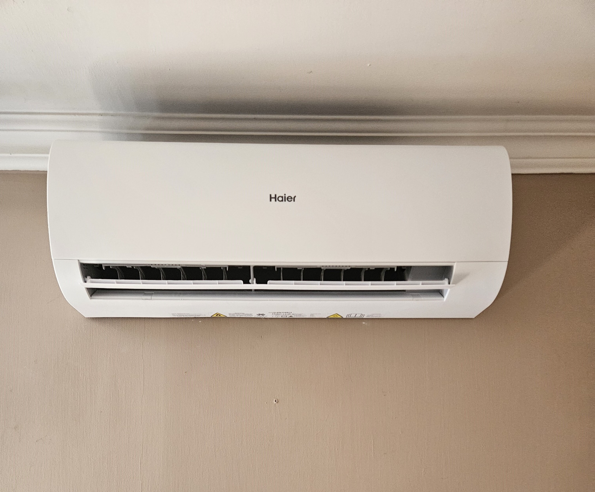 Biały klimatyzator Haier zamontowany na beżowej ścianie pod sufitem z ozdobną listwą.