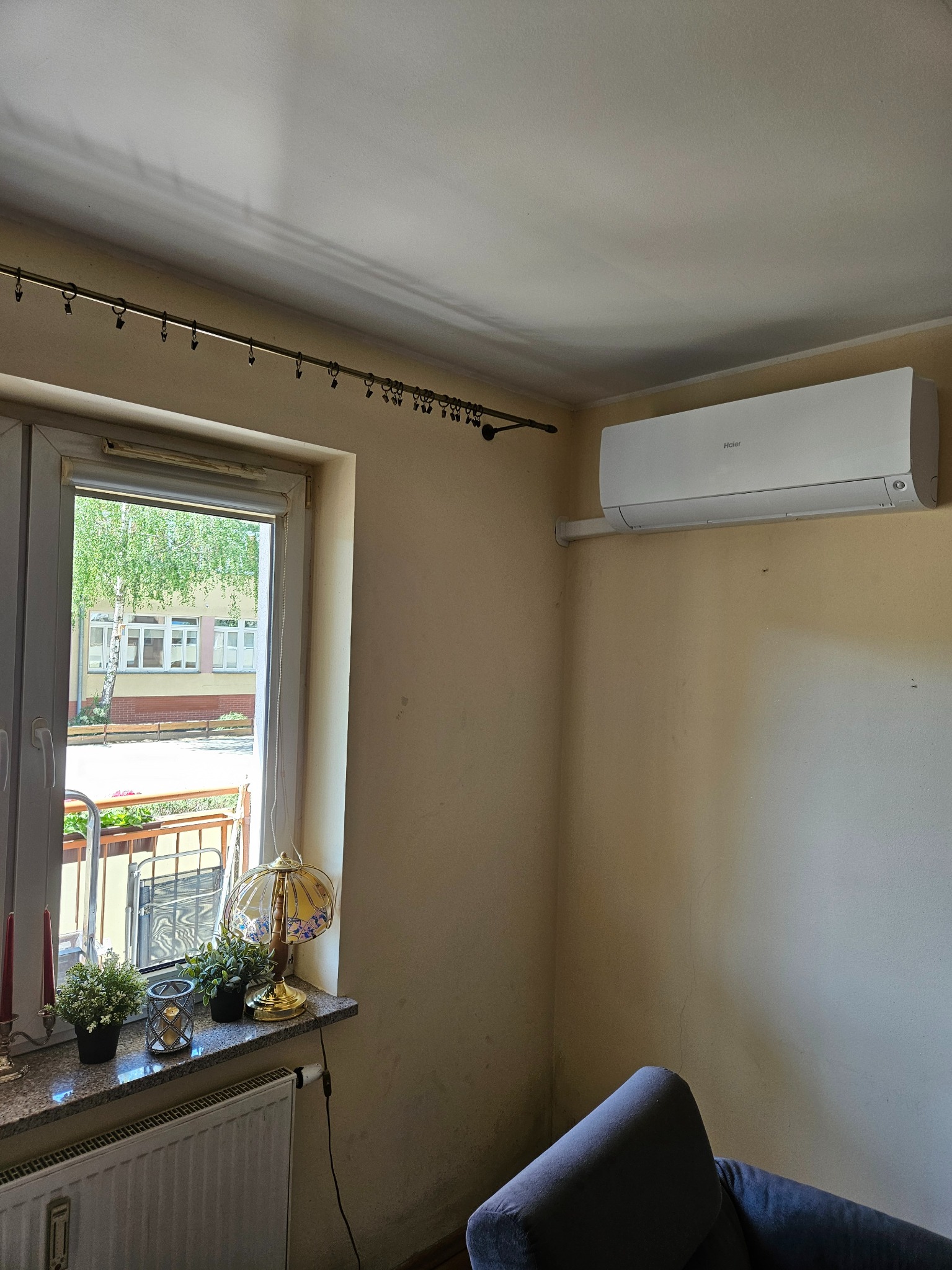 Klimatyzator Haier zamontowany w pokoju z widokiem na budynek przez okno w Gorzowie Wielkopolskim. Na parapecie lampka i kwiaty.