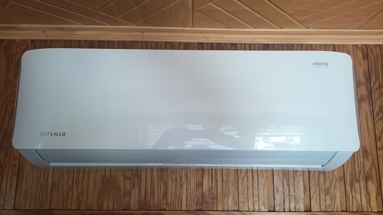 Biała jednostka wewnętrzna klimatyzacji Rotenso zamontowana na ścianie wyłożonej boazerią z pionowych paneli drewnianych.