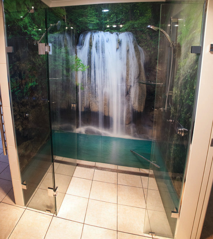 Szklana kabina prysznicowa z fototapetą wodospadu, chromowana armatura, płytki podłogowe w odcieniach beżu.