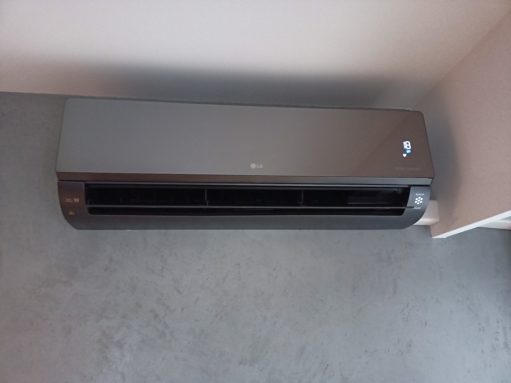 Szary klimatyzator LG zamontowany na szarej ścianie w mieszkaniu w Poznaniu, widoczny wyświetlacz temperatury i logo producenta.