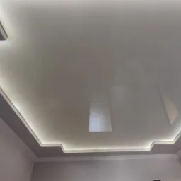 Biały, podwieszany sufit z oświetleniem LED wzdłuż krawędzi, z widocznym fragmentem ozdobnej listwy przysufitowej.