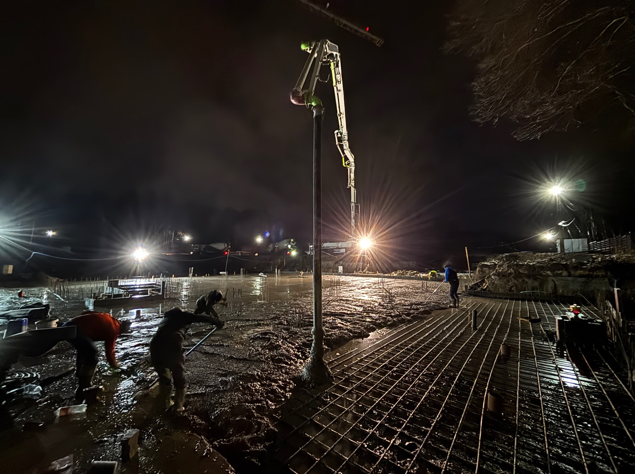 Nocne wylewanie posadzki przemysłowej z użyciem pompy do betonu; widoczne zbrojenie i pracownicy w trakcie rozprowadzania betonu.