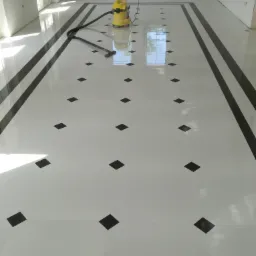 Błyszcząca, biała podłoga z czarnymi, kwadratowymi akcentami i czarną obwódką w przestronnym pomieszczeniu w Wyszkowie, czyszczona żółtym odkurzaczem przemysłowym.