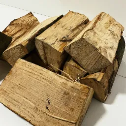 Stos pociętych, suchych klocków drewna ułożonych na białym podłożu, widoczne sęki i fragmenty kory.