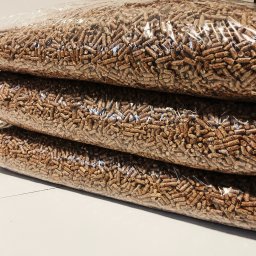 KMMOBILI Krystian Miętka - Ułożone jeden na drugim przezroczyste worki wypełnione brązowym granulatem drzewnym, widoczne z bliska na białym tle.