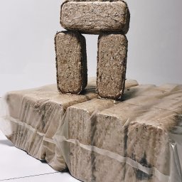 KMMOBILI Krystian Miętka - Ułożone w piramidę prostokątne kostki brykietu drzewnego, część zafoliowana, na białym tle.