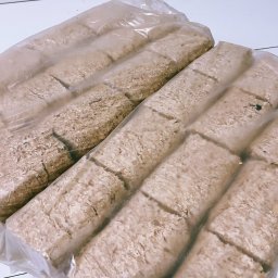 KMMOBILI Krystian Miętka - Dwa pakiety brykietu drzewnego ułożone obok siebie, każdy podzielony na segmenty, zapakowane w przezroczystą folię.