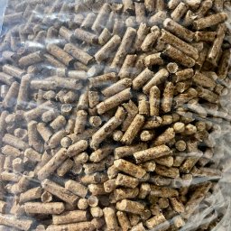 KMMOBILI Krystian Miętka - Bliski kadr na przezroczysty worek wypełniony brązowymi, cylindrycznymi granulkami, prawdopodobnie biopaliwa, z widocznymi drobnymi włóknami drzewnymi.