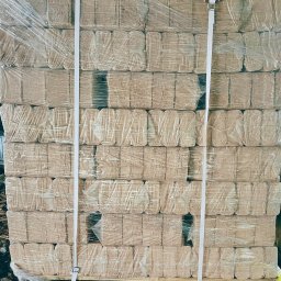 KMMOBILI Krystian Miętka - Ułożone na palecie i owinięte folią bloki brykietu drzewnego, zabezpieczone taśmą transportową.