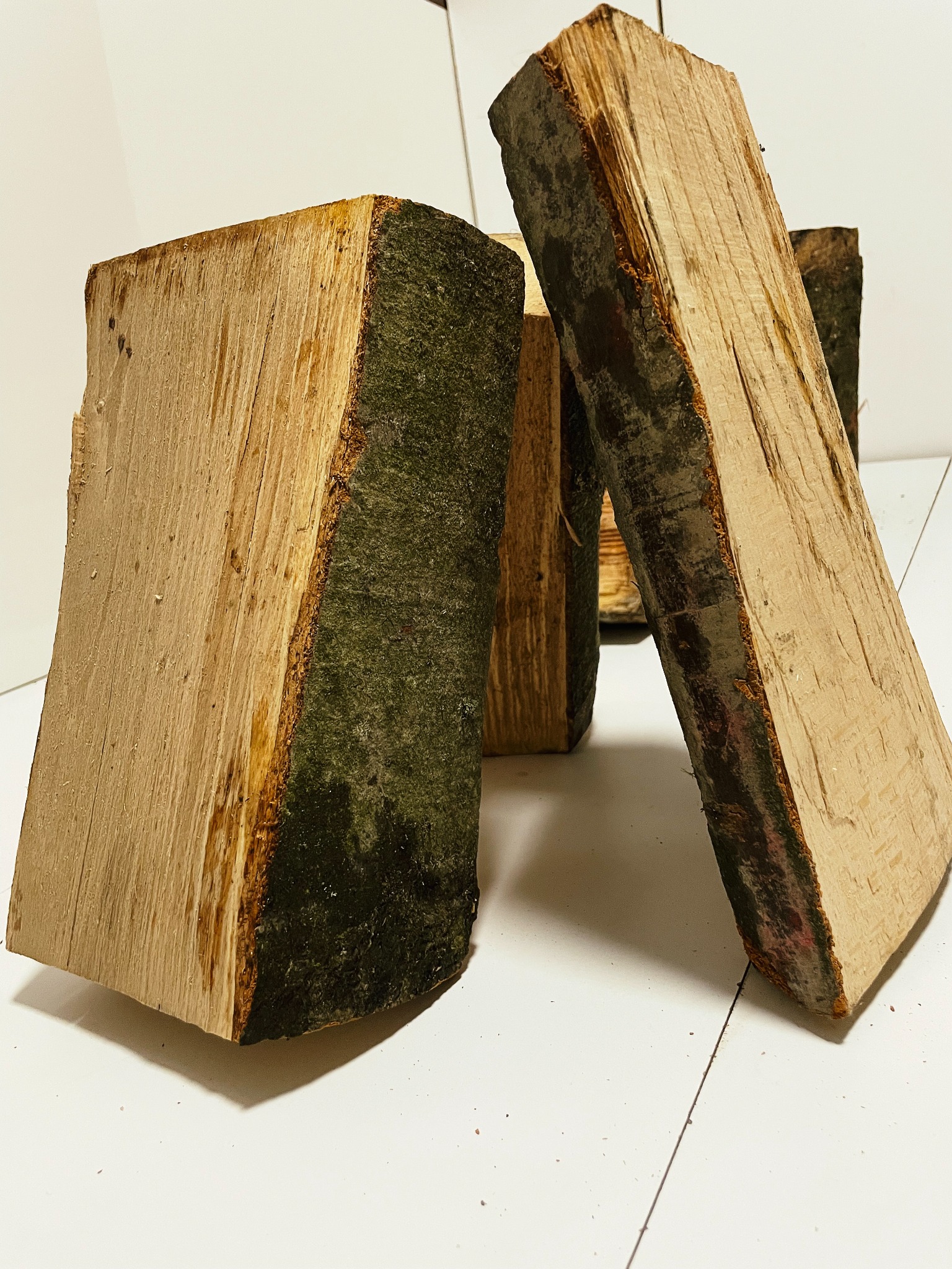 Kilkakrotnie pocięte, prostokątne kawałki drewna z korą, ustawione pionowo na białym tle.