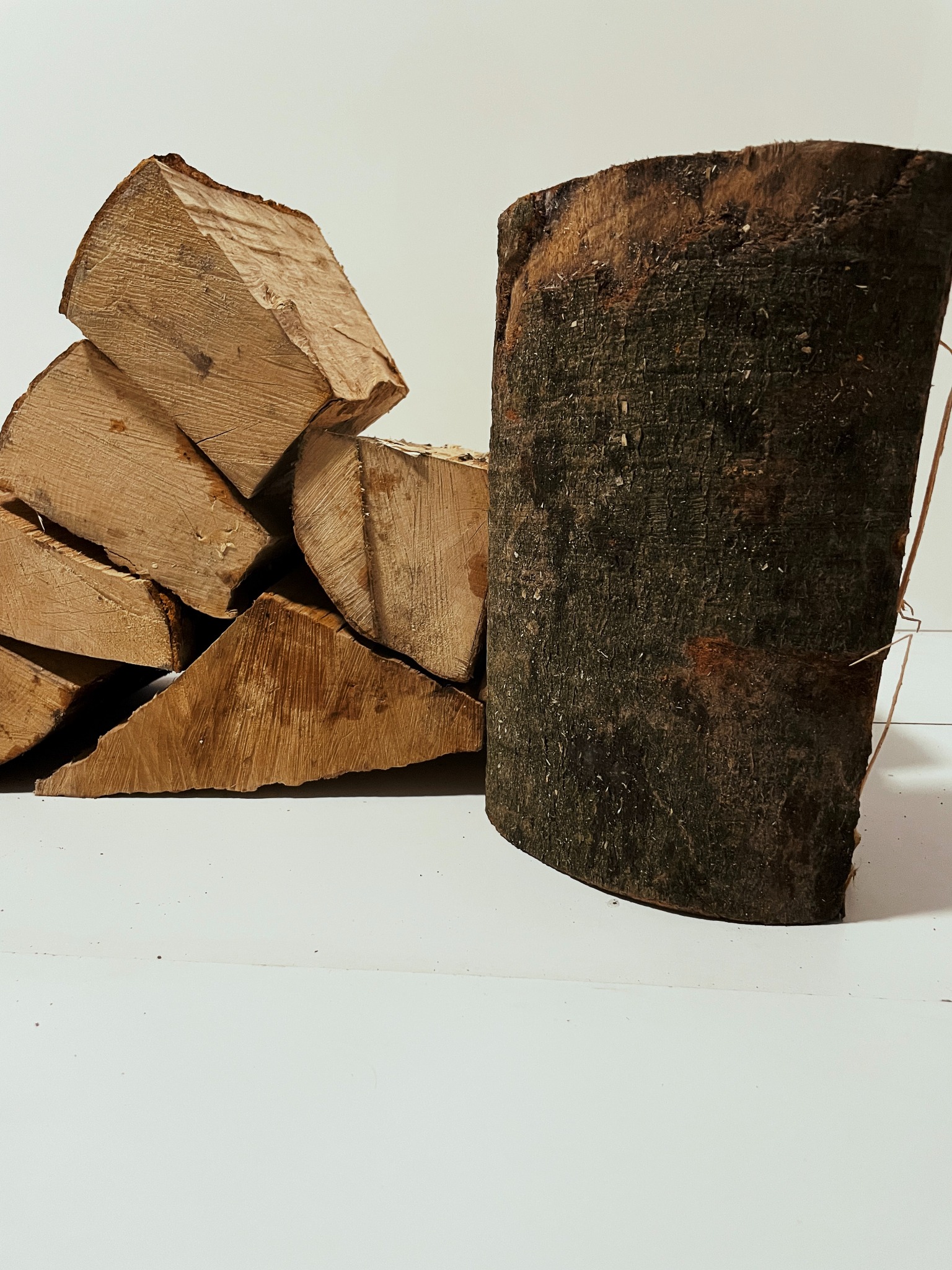 Stos pociętego drewna opałowego z widocznymi słojami, obok pionowy kawałek drewna z korą, na białym tle.