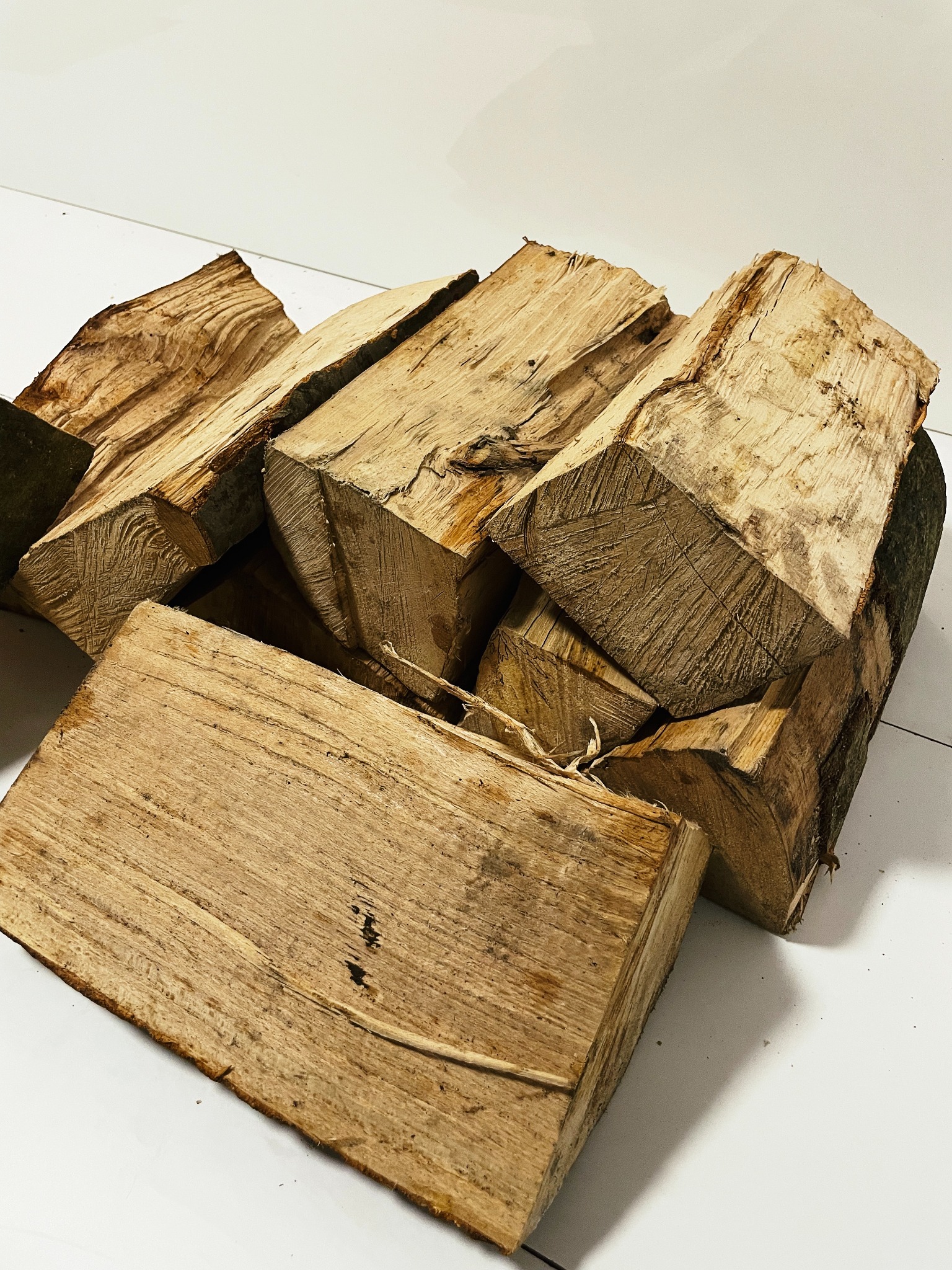 Stos pociętych, suchych klocków drewna ułożonych na białym podłożu, widoczne sęki i fragmenty kory.