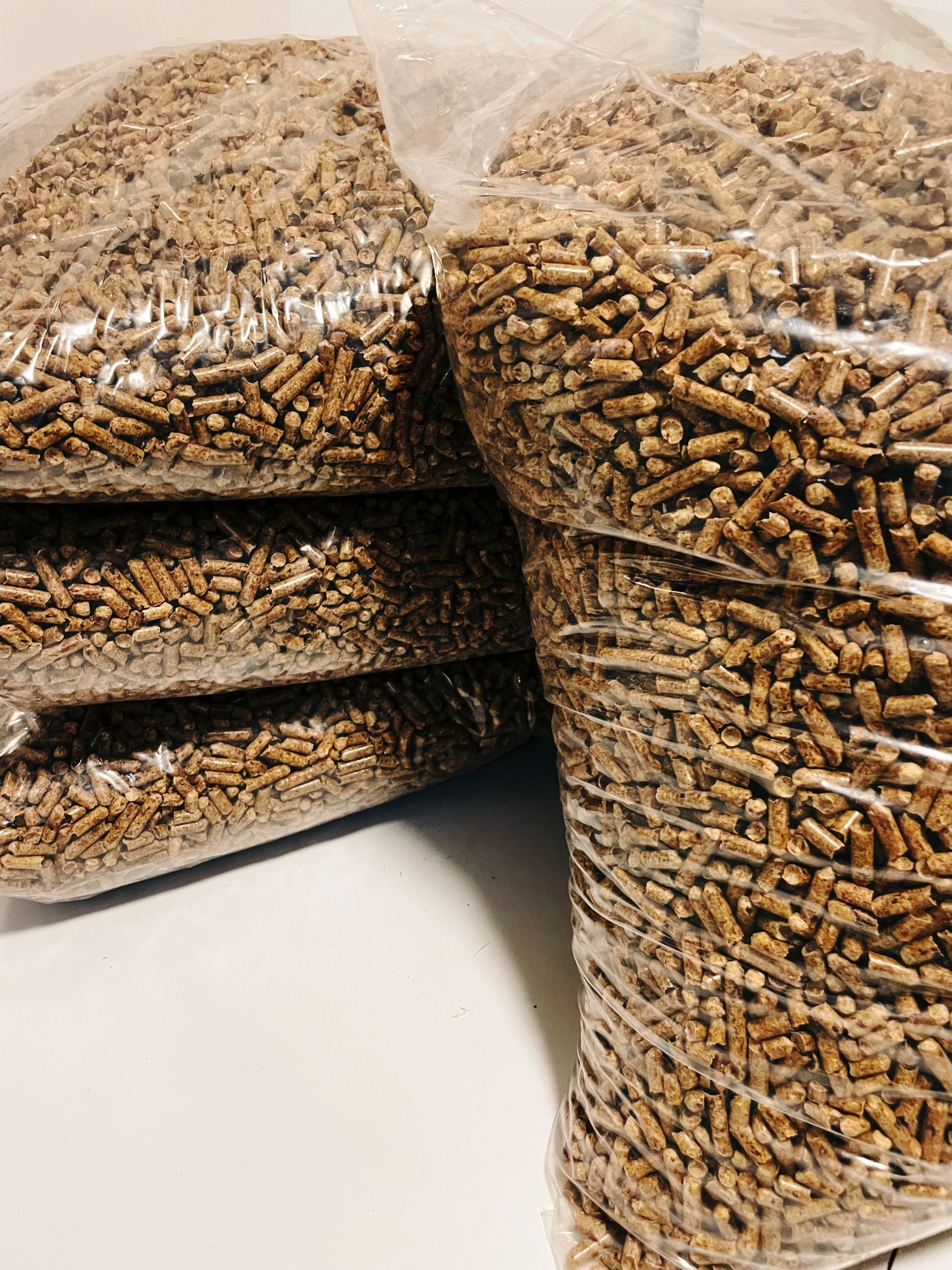 Ułożone worki z pelletem drzewnym, widoczne przez przezroczyste opakowanie, na białym tle.