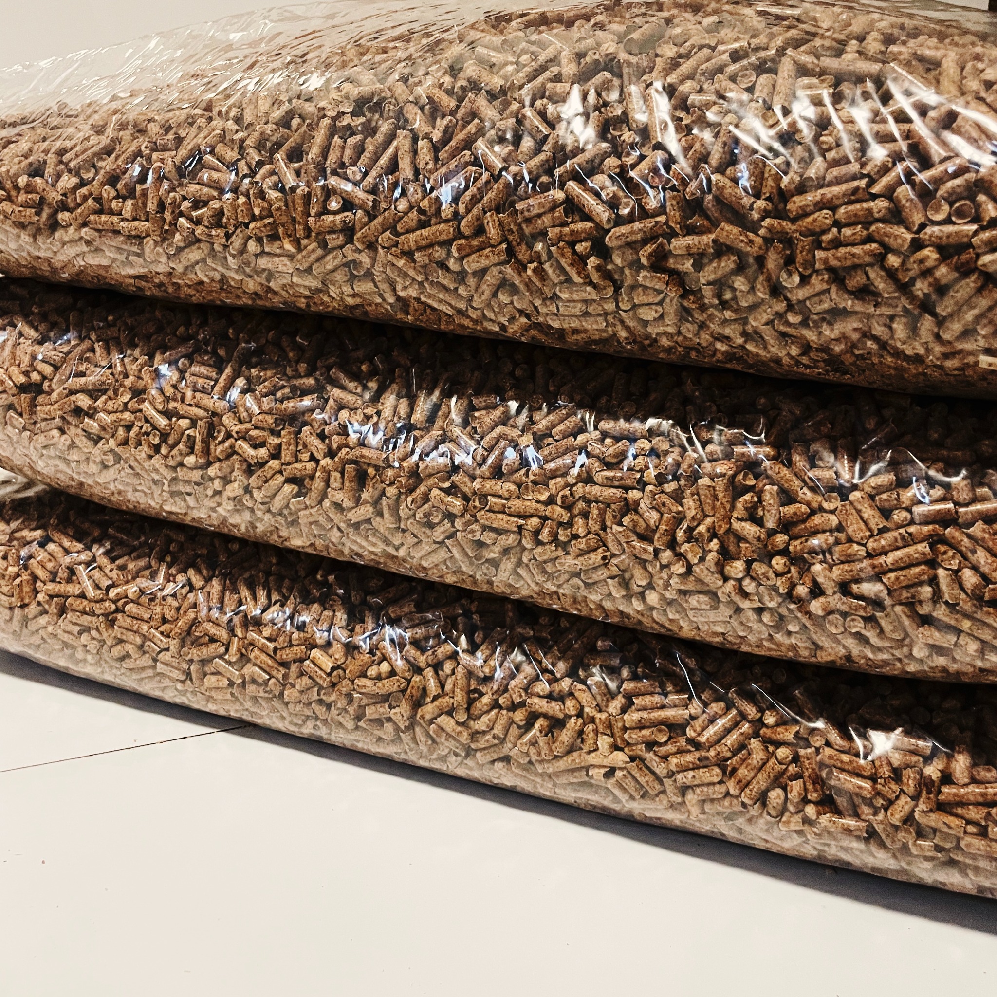 Ułożone jeden na drugim przezroczyste worki wypełnione brązowym granulatem drzewnym, widoczne z bliska na białym tle.