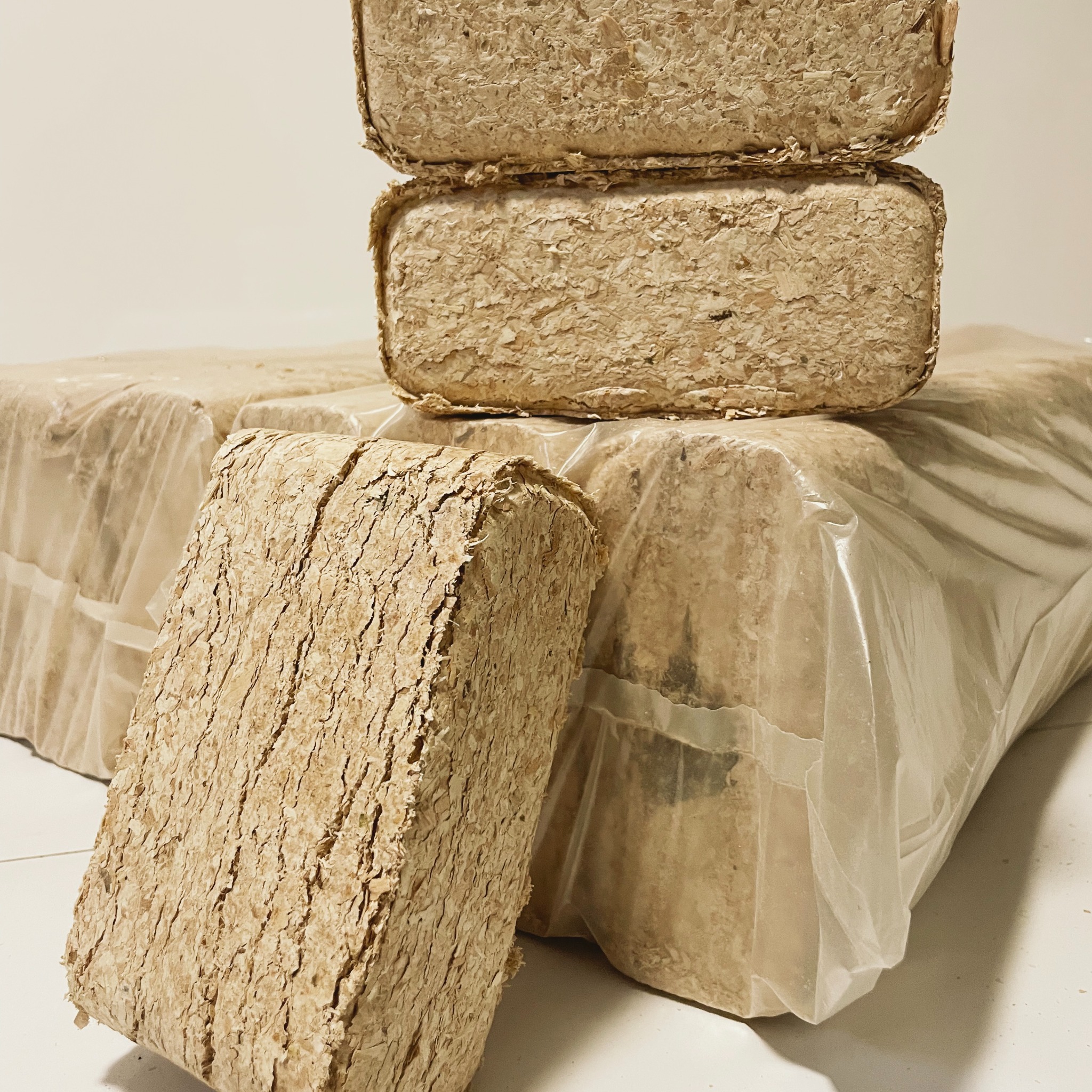 Stos ułożonych kostek brykietu drzewnego z widoczną teksturą włókien drzewnych, część zapakowana w przezroczystą folię.