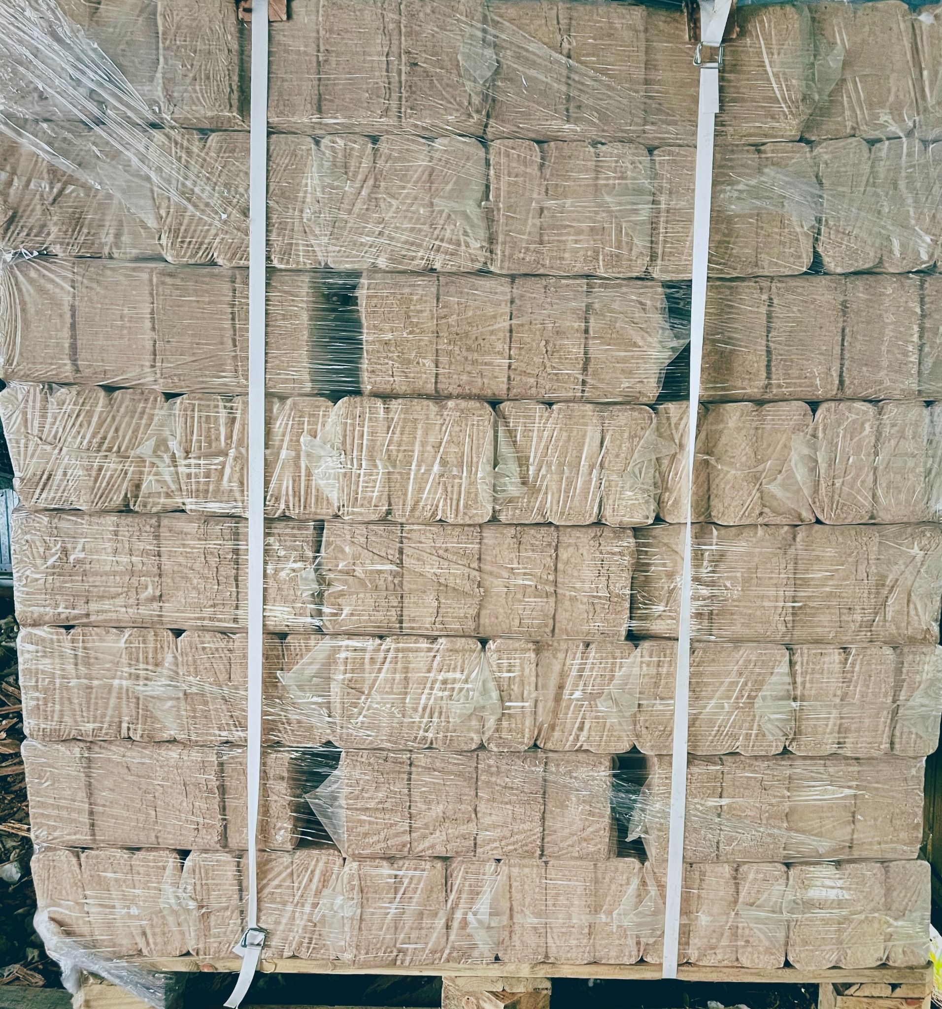 Ułożone na palecie i owinięte folią bloki brykietu drzewnego, zabezpieczone taśmą transportową.