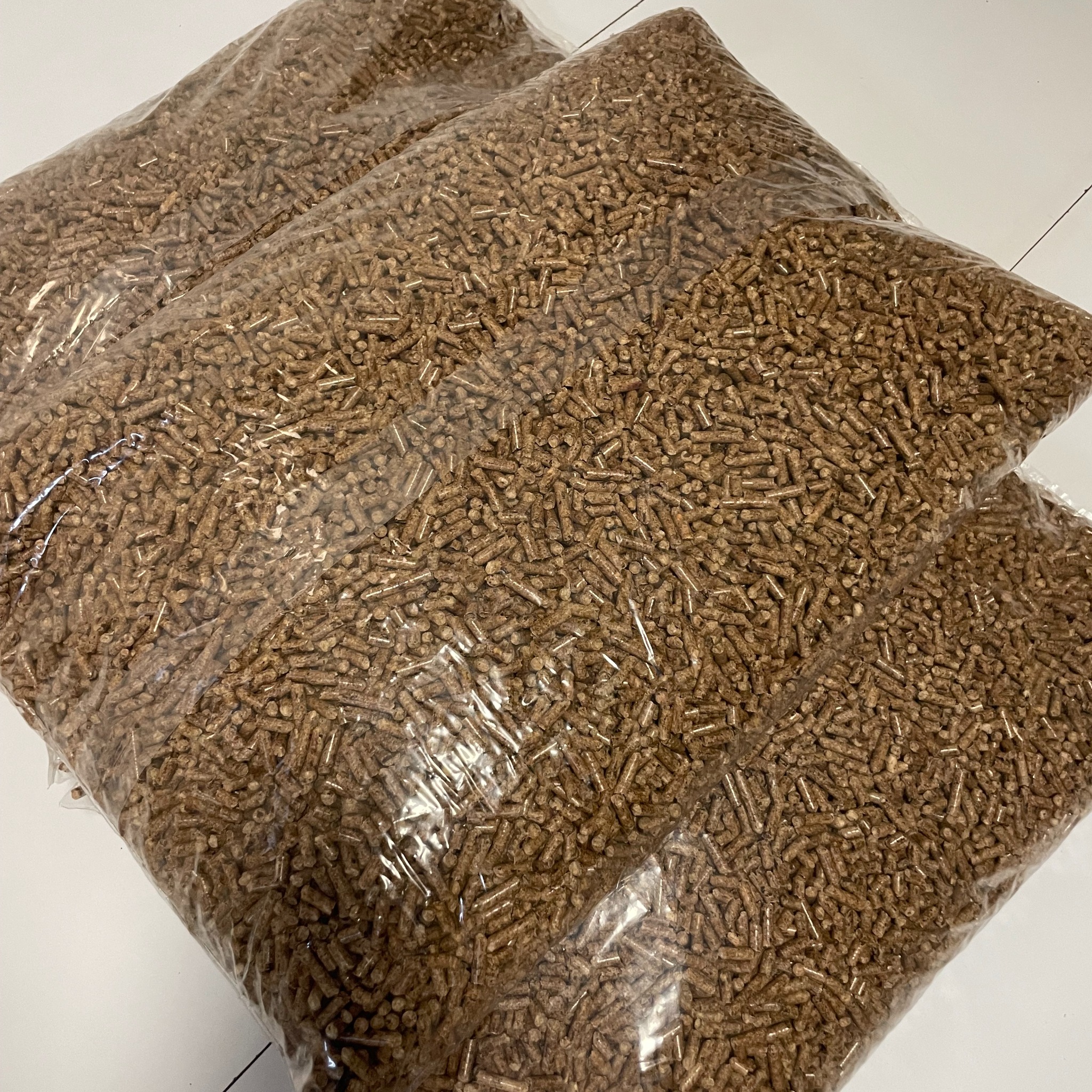 Dwa przezroczyste worki wypełnione brązowymi, drobnymi granulkami na białym tle, prawdopodobnie paliwo ekologiczne.