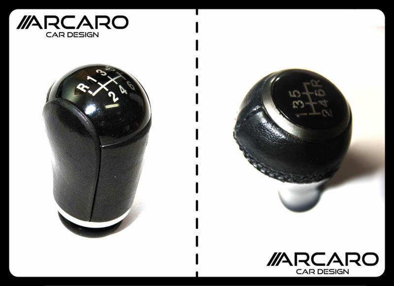 Dwie gałki zmiany biegów: jedna z czarną skórzaną osłoną i białą podstawą, druga z czarną skórzaną osłoną obszytą drobnymi przeszyciami, obie z wyraźnie widocznymi oznaczeniami biegów na górze...