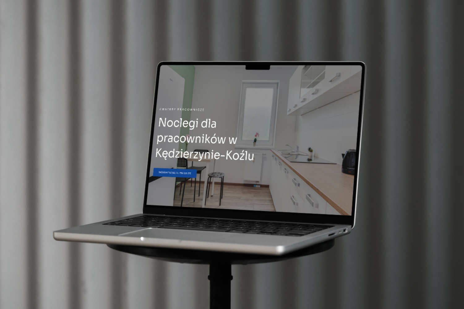 Laptop wyświetlający stronę internetową z ofertą noclegów pracowniczych w Kędzierzynie-Koźlu, widoczna jasna kuchnia w tle.