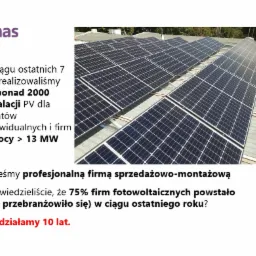 Instalacja fotowoltaiczna na dachu budynku, widok z góry pod kątem, panele ułożone w rzędach, częściowo zacienione, z widocznymi elementami konstrukcyjnymi.