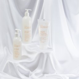 PFH KATARZYNA SOŁTYSIAK - Stylizowana fotografia produktowa: Trzy białe kosmetyki Ziaja Naturalnie Pielęgnujemy na tle białej, połyskującej tkaniny. Żel do higieny intymnej, żel do twarzy i szampon.