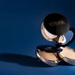 Stylizowana fotografia produktowa: dwa pudry Eveline Cosmetics ułożone jeden na drugim na niebieskim tle, z widocznym odbiciem i cieniem.