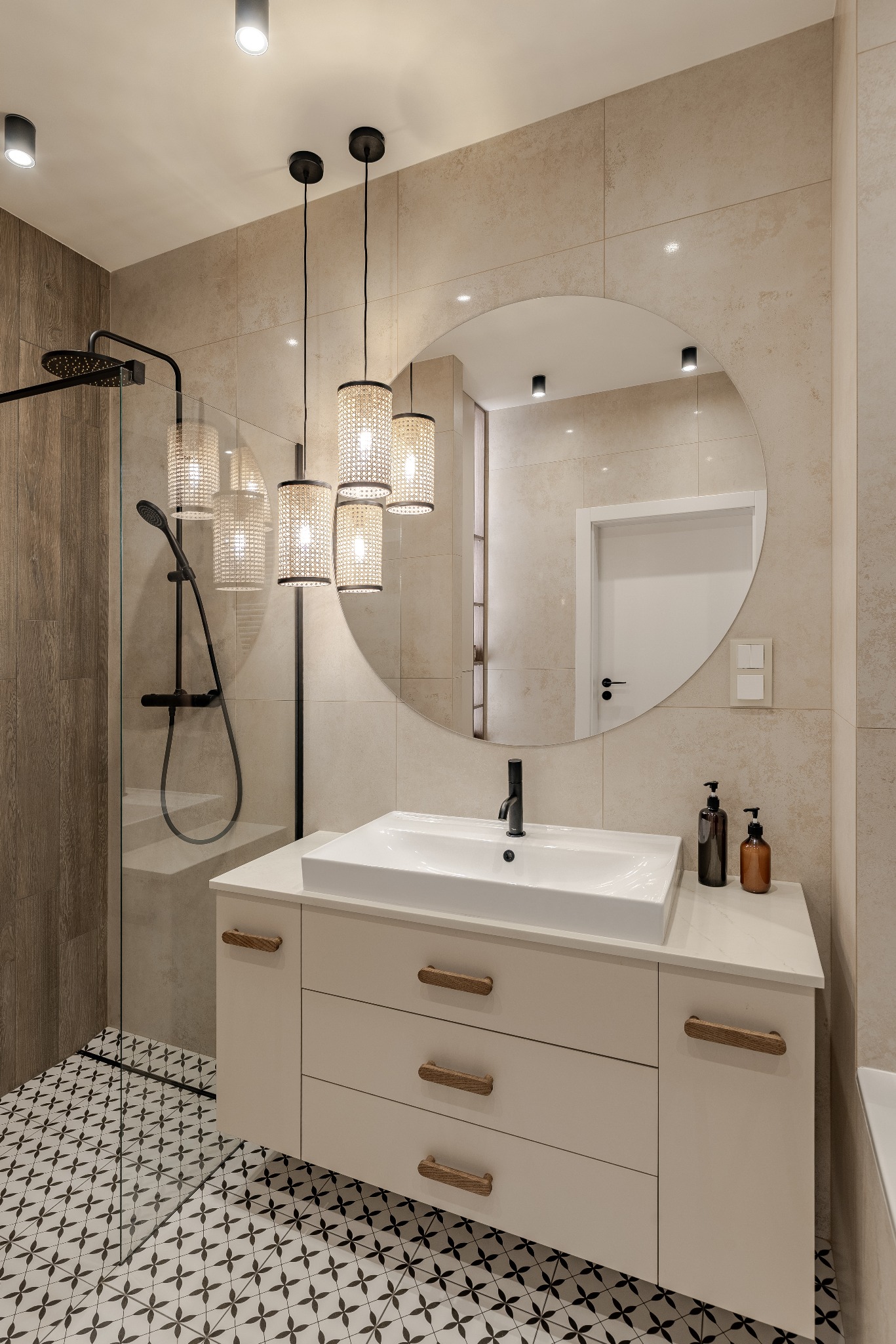 Nowoczesna łazienka z kabiną prysznicową typu walk-in, okrągłym lustrem i wiszącą szafką z umywalką. Uwagę zwracają lampy z abażurami z plecionki.