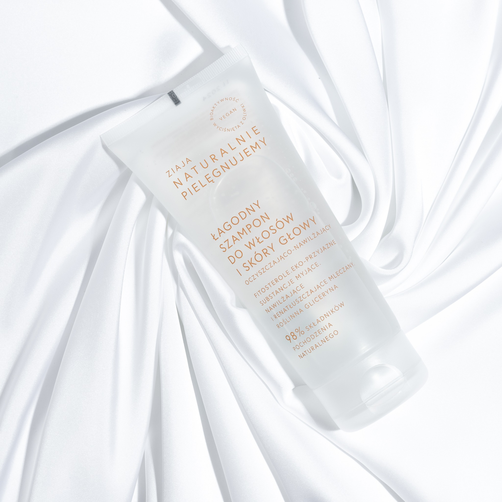 Stylizowana fotografia produktowa: tuba szamponu ZIAJA na białym, drapowanym tle. Minimalistyczny design, stonowana kolorystyka, subtelne światło podkreśla naturalność produktu.