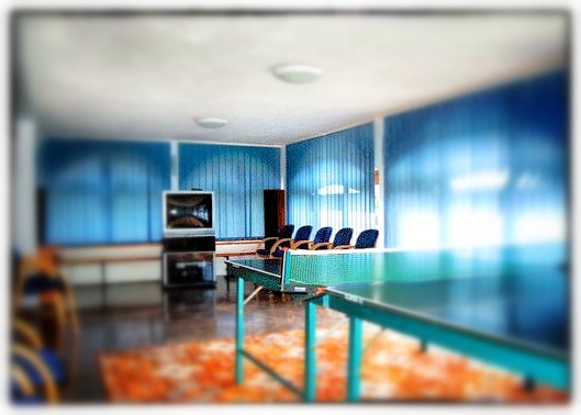 Sala z niebieskimi zasłonami, stołem do ping-ponga i telewizorem, potencjalnie w ośrodku terapeutycznym.