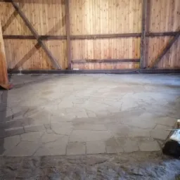 Układanie nieregularnych płyt kamiennych na podłodze wewnątrz budynku z drewnianą konstrukcją ścian.