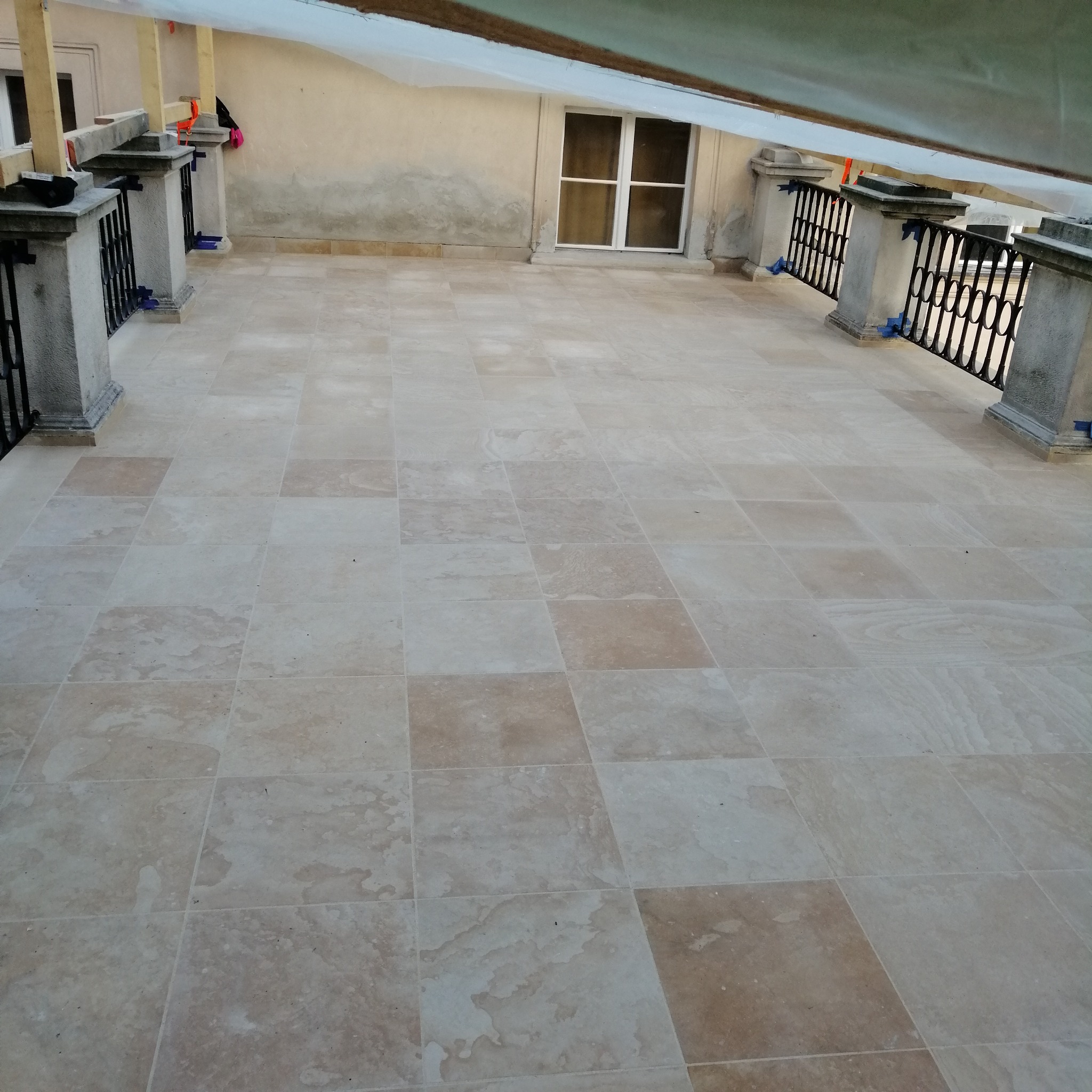 Jasny taras z kamiennych płyt ułożonych w kwadraty, z balustradą z metalowymi elementami i kamiennymi słupkami, widok z góry.