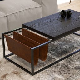 P&M Pracownia Mateusz Ługowski - Nowoczesny stolik kawowy z ciemnym blatem, metalową ramą i skórzanymi przegródkami na czasopisma, obok jasnej sofy, z słuchawkami na blacie.