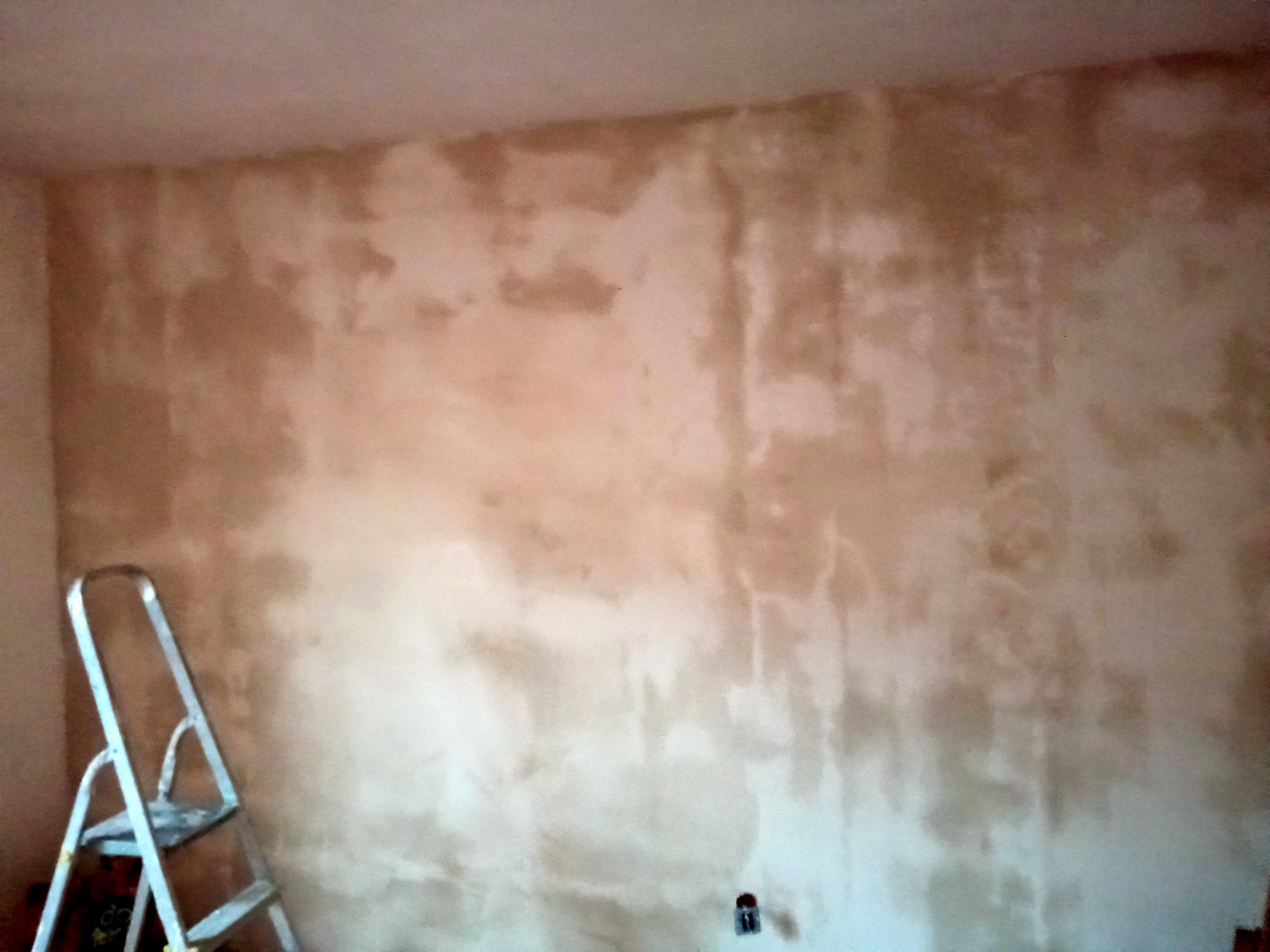 Ściana w trakcie prac wykończeniowych z widocznymi niedoskonałościami i śladami po nałożonym materiale, drabina malarska z lewej strony kadru.