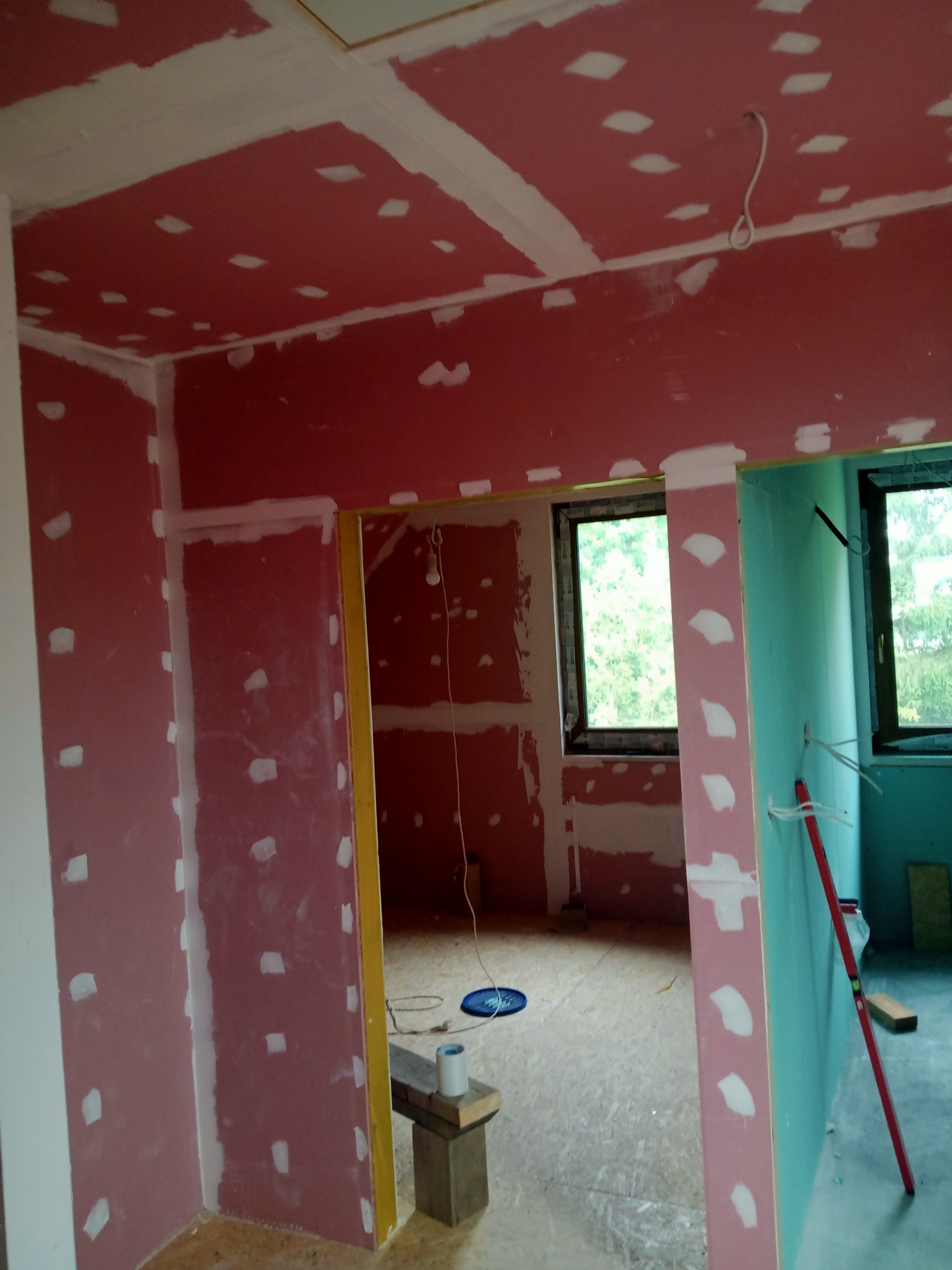 Wnętrze w trakcie wykańczania: ściany i sufit pokryte płytami kartonowo-gipsowymi z widocznymi miejscami łączeń przygotowanymi do szpachlowania, widoczne przewody elektryczne, poziomica oparta...