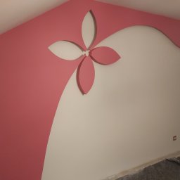 Sevma Art Sebastian Czerwinski - Dekoracyjne malowanie ściany z motywem kwiatowym w kolorze różowym i białym, widoczny fragment sufitu i podłogi w remontowanym pomieszczeniu.