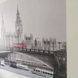 Fototapeta przedstawiająca czarno-biały widok na Londyn z czerwonym autobusem na moście, naklejona na jasnej ścianie.