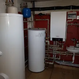 Instalacja kotła grzewczego Viessmann z zasobnikami ciepłej wody w pomieszczeniu z czerwonymi ścianami i licznymi rurami.