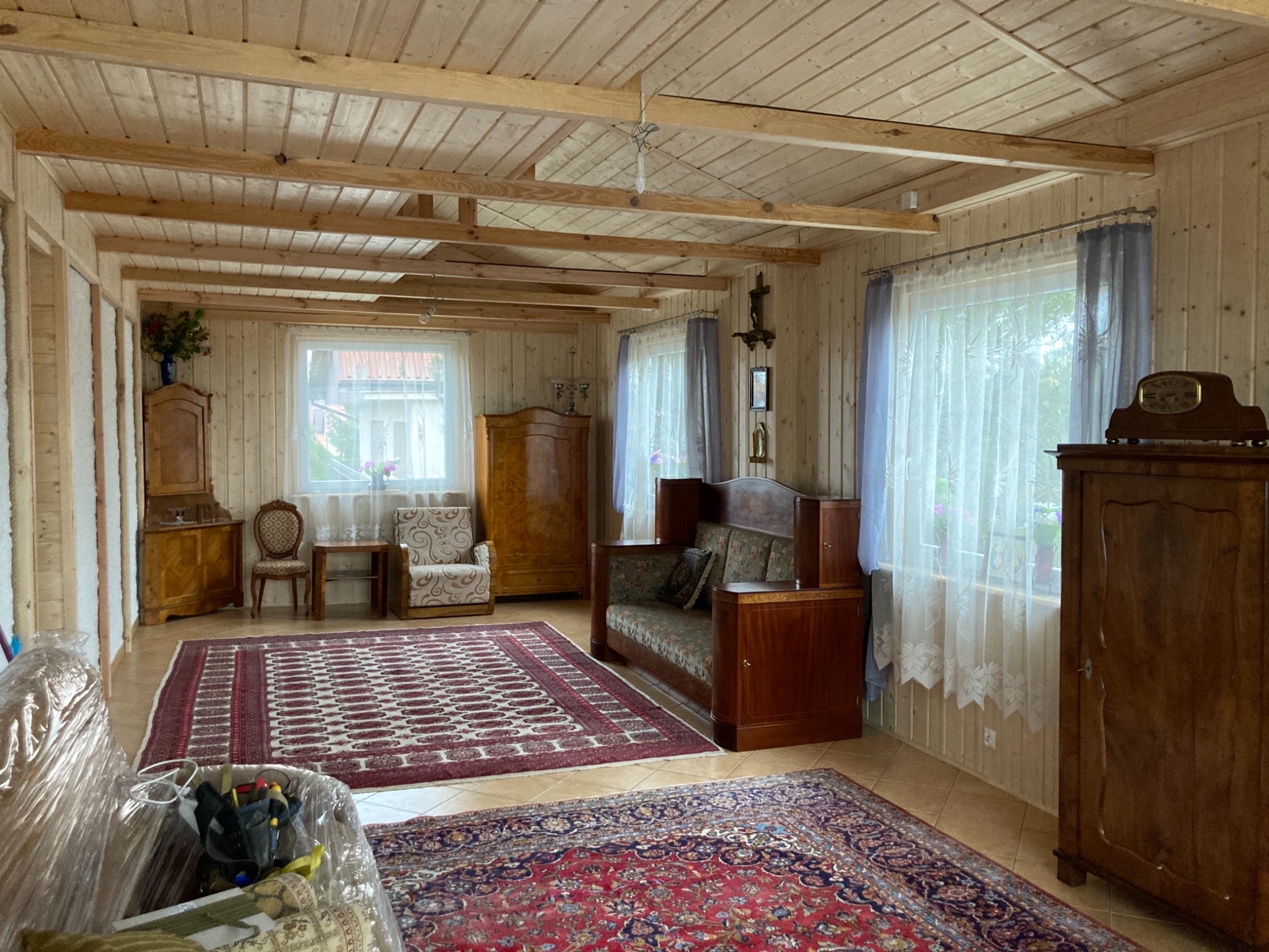 Wnętrze domu z drewnianą boazerią, widoczny sufit z belek, meble w stylu retro i dywany orientalne.