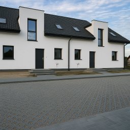 Metrikum Aleksander Atraszkiewicz - Szara ażurowa kostka na podjeździe przed szeregowcem z białymi ścianami i czarną stolarką okienną. Minimalistyczny design.