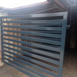 Kakadu - Szara, stalowa brama przesuwna z poziomymi szczeblami, świeżo po malowaniu, w warsztacie.