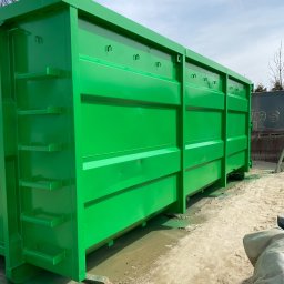 Kakadu - Duży, metalowy kontener na gruz w jaskrawo zielonym kolorze, świeżo po malowaniu, stojący na piaszczystym podłożu.
