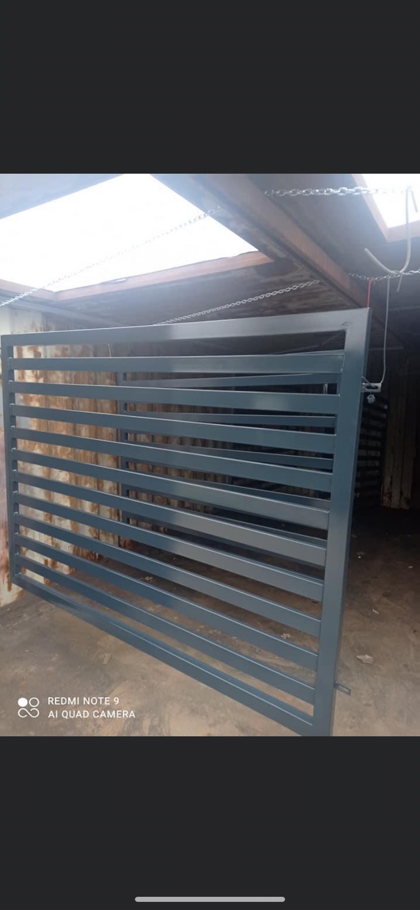 Szara, stalowa brama przesuwna z poziomymi szczeblami, świeżo po malowaniu, w warsztacie.