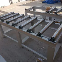 Dwie metalowe konstrukcje z rolkami, prawdopodobnie stoły robocze lub elementy linii produkcyjnej, z widocznymi śladami spawania i obróbki metalu.