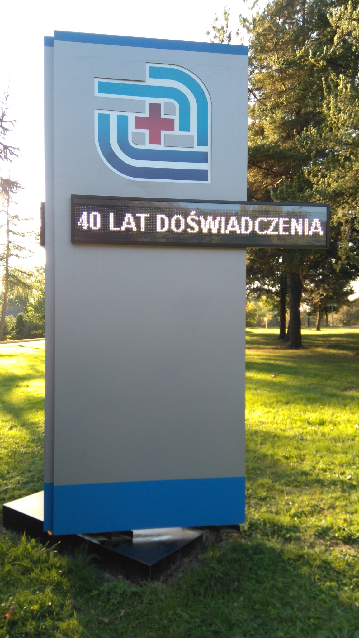 Pylon reklamowy z logo i wyświetlaczem LED wskazującym 40 lat doświadczenia, umieszczony na tle zielonego trawnika i drzew