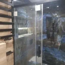 Nowoczesna kabina prysznicowa z szklanymi drzwiami i panelami w odcieniach granatu i błękitu, z czarnymi elementami wykończeniowymi i grzejnikiem drabinkowym po lewej stronie.