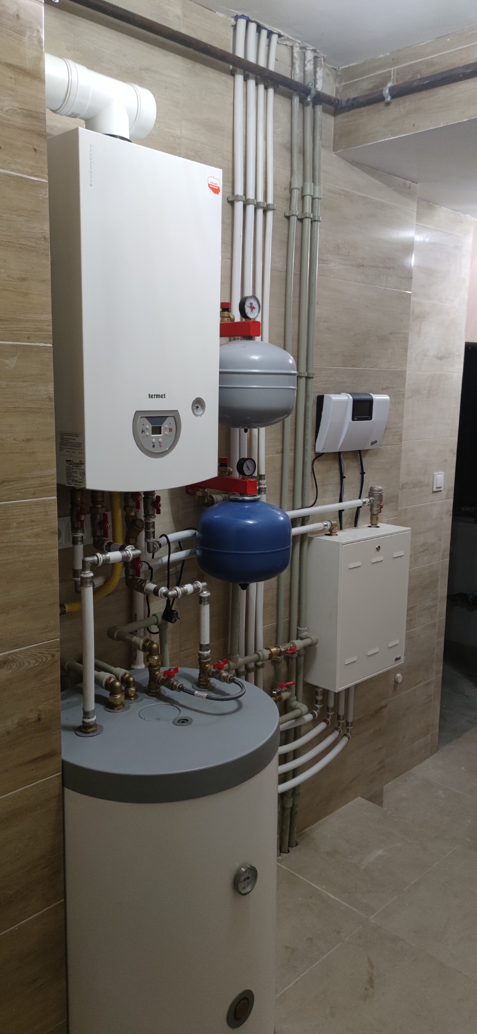 Kotłownia z zamontowanym piecem gazowym Termet, zbiornikiem na wodę, naczyniami przeponowymi i rozbudowaną instalacją z rur miedzianych i plastikowych na tle wykończonych w płytkach ścian i podłogi.
